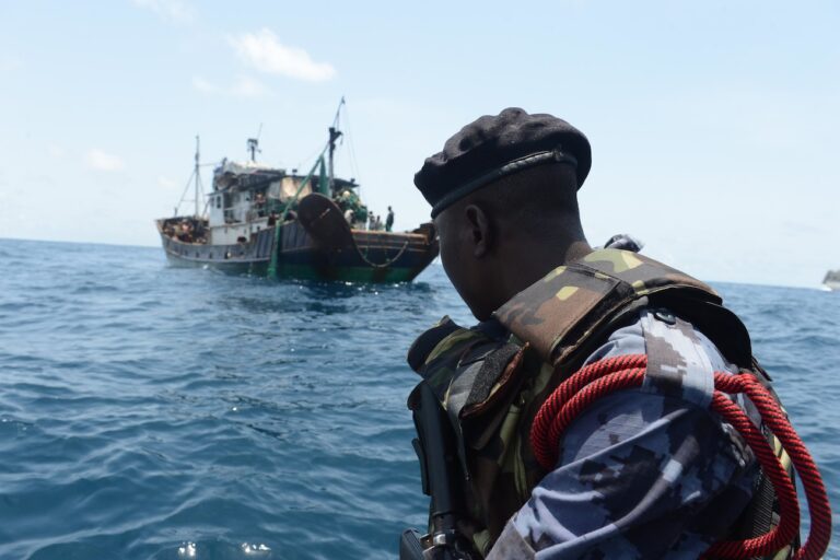 A member of the Ghanaian maritime police observes a vessel suspected of fishing illegally prior to boarding it as part of a U.S.-Ghana combined maritime law enforcement operation in 2014. Image courtesy of Commander, U.S. Naval Forces Europe-Africa/U.S. 6th Fleet via Flickr (CC BY-ND 2.0 Deed).