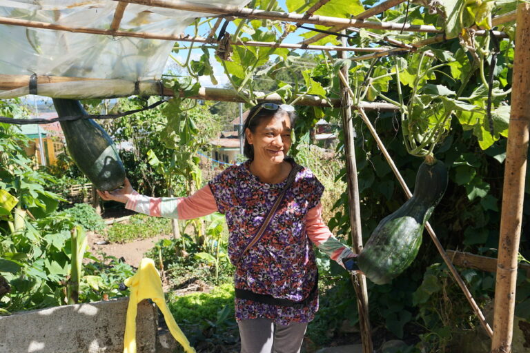 Grael Bomowey poses with a fruiting butternut squash grown by her neighbor after receiving a seed from her collection. Image by Laurie Mae Gucilatar.