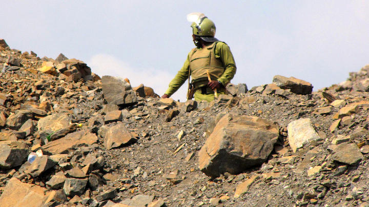 Tanzanian police officer in dull green riot gear and helmet, pictured against the sky guarding waste dump site at Barrick Gold's North Mara mine. Image courtesy Catherine Coumans / Mining Watch.