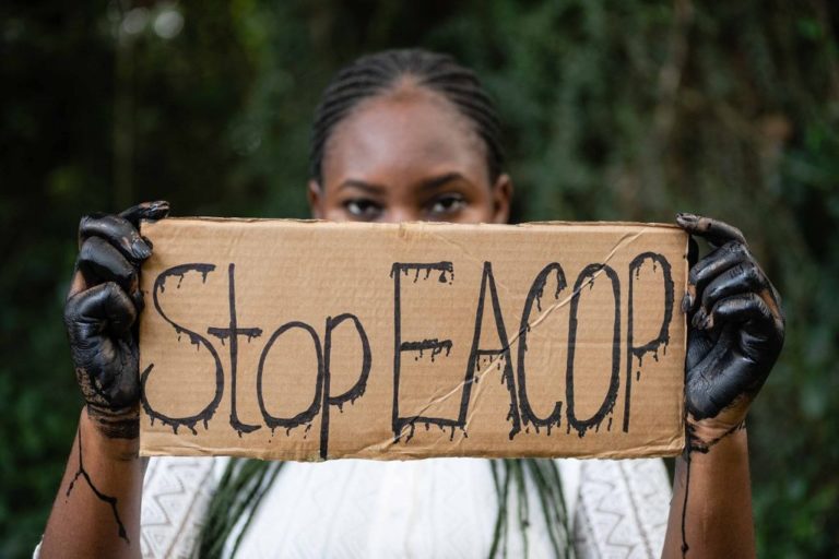 Person holding cardboard sign saying Stop EACOP", concealing lower half of their face. Photothèque AT via Flickr (CC BY-NC 2.0)